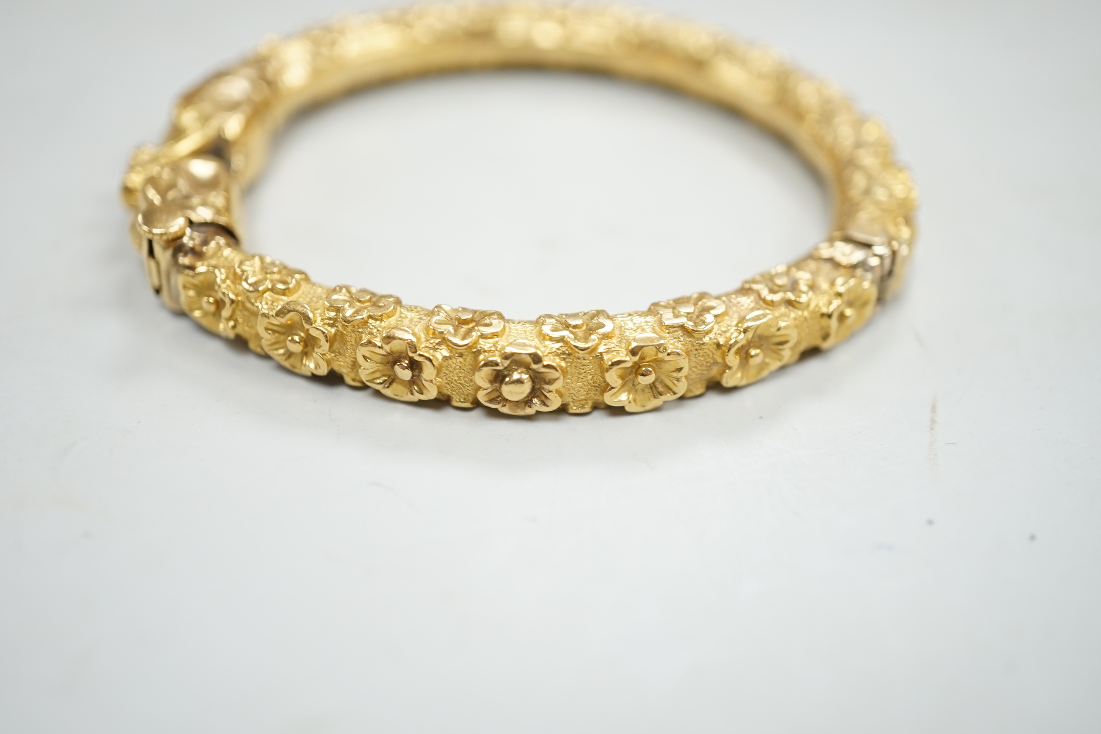 An antique yellow metal hinged bangle, with flower head decoration and dragon's? head terminals, gross weight 23.9 grams.